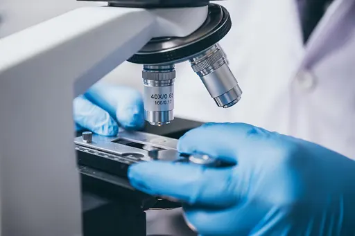 A lab technician studies a sample underneath a microscope