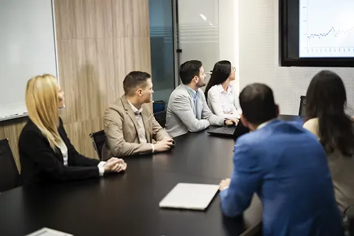 Investors sit around table watching a presentation on the screen