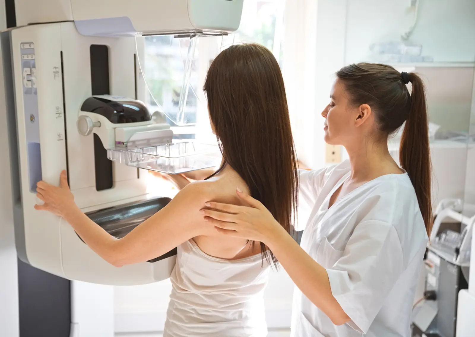 A healthcare professional assists a patient during a mammogram procedure, highlighting the importance of breast cancer screening. The image depicts the patient positioned in front of a mammography machine, with the technician providing guidance and support.